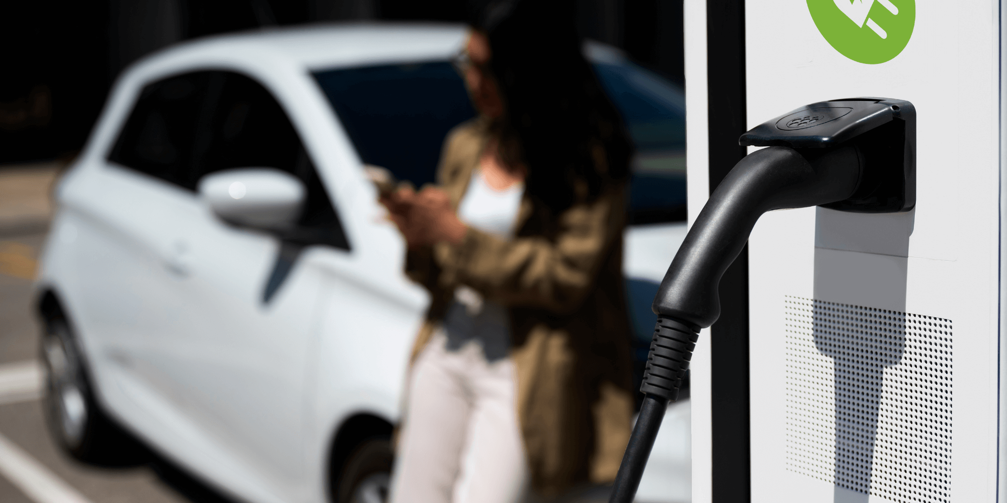 femme qui attend que sa voiture charge à une borne électrique